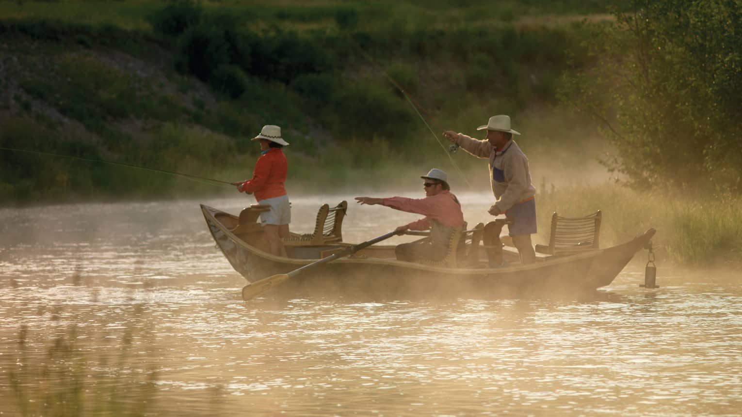 Mist rises from river over three people in fishing boat, one pointing to water