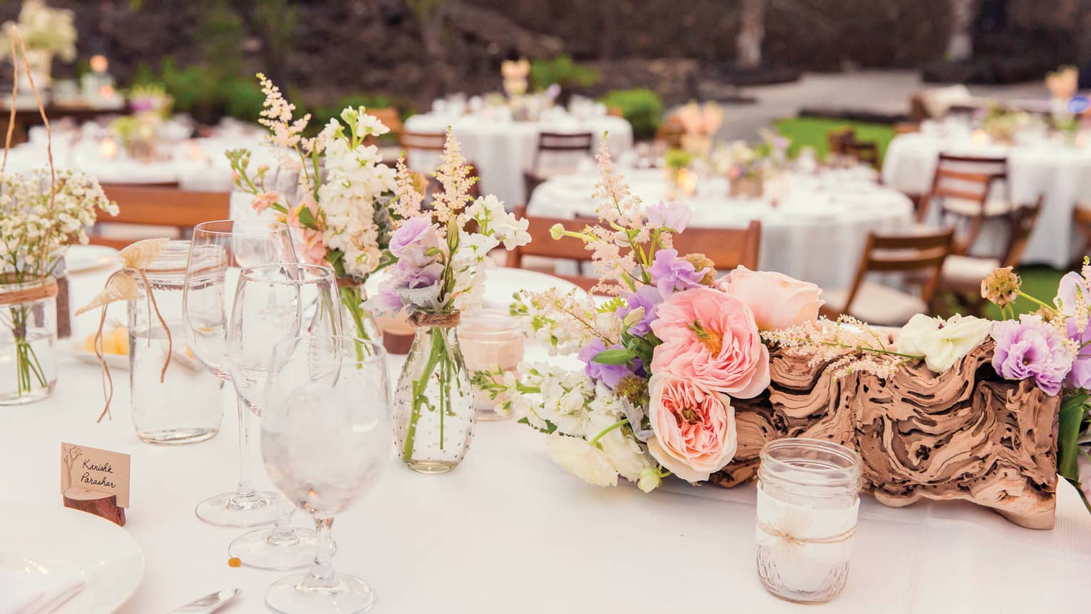 Outdoor wedding reception dining table with pink and purple flowers, glass jars