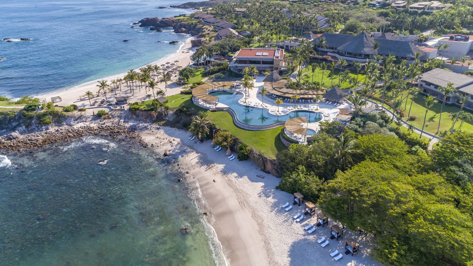 An aerial view of a beach shore with a large property on it with an outdoor pool.