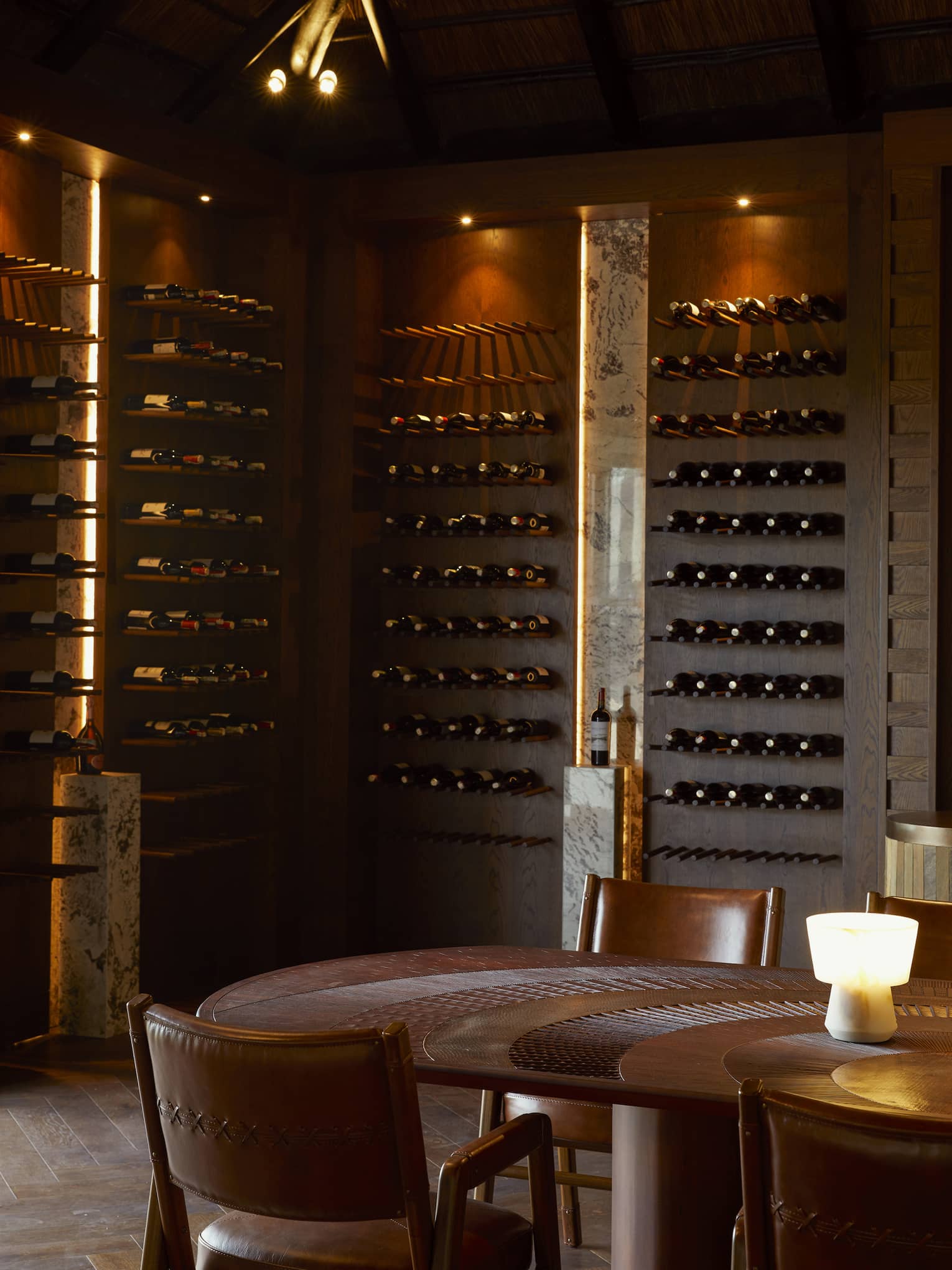 Dimly lit wine cellar with bottles lining dark wooden walls and round table in centre