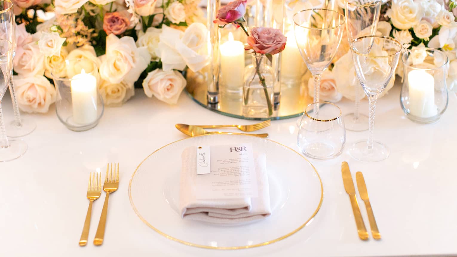 A clear and gold plate next to candles and flowers.