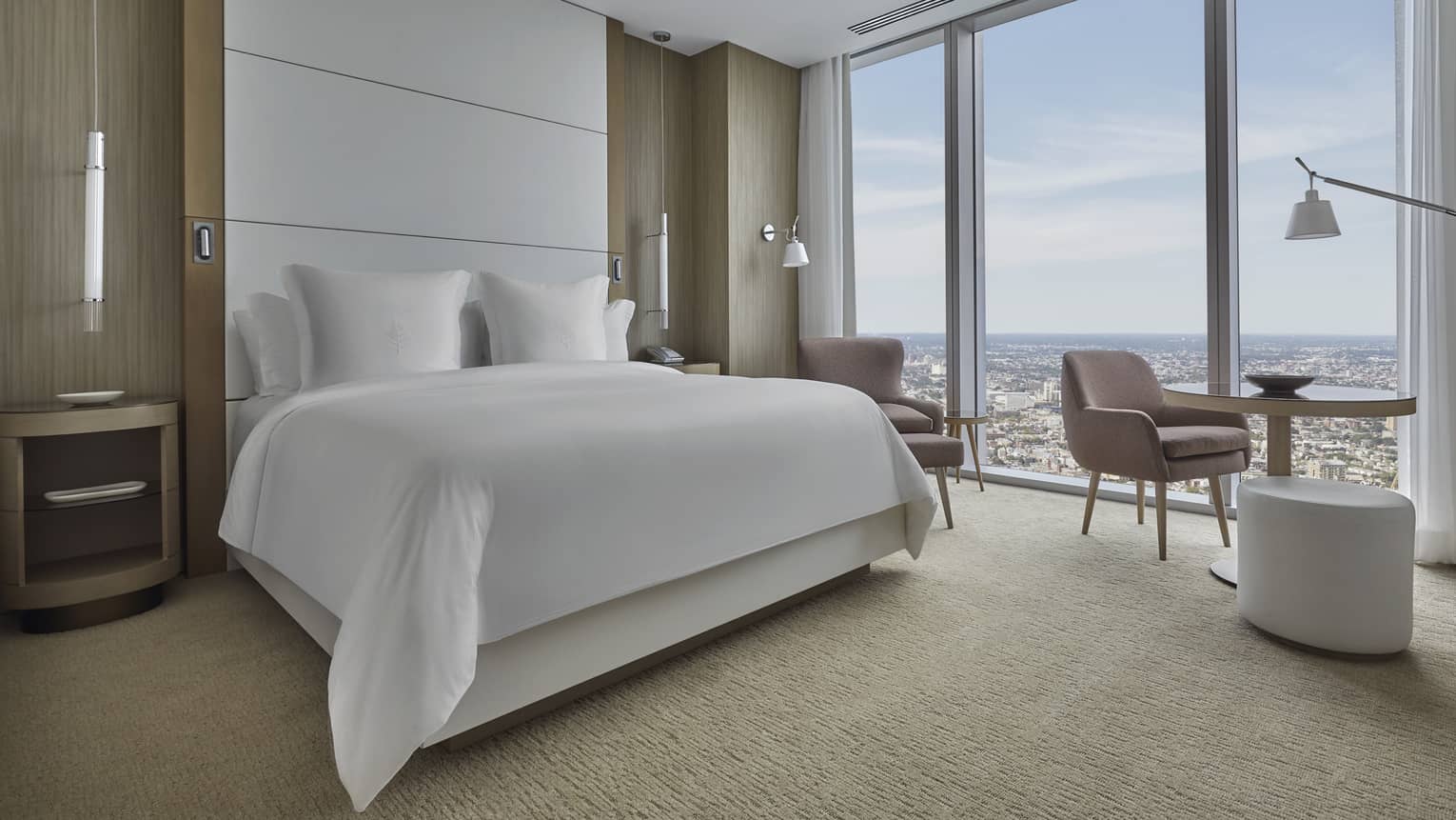 Bedroom with king bed, floor-to-ceiling headboard, arm chair and wall of windows