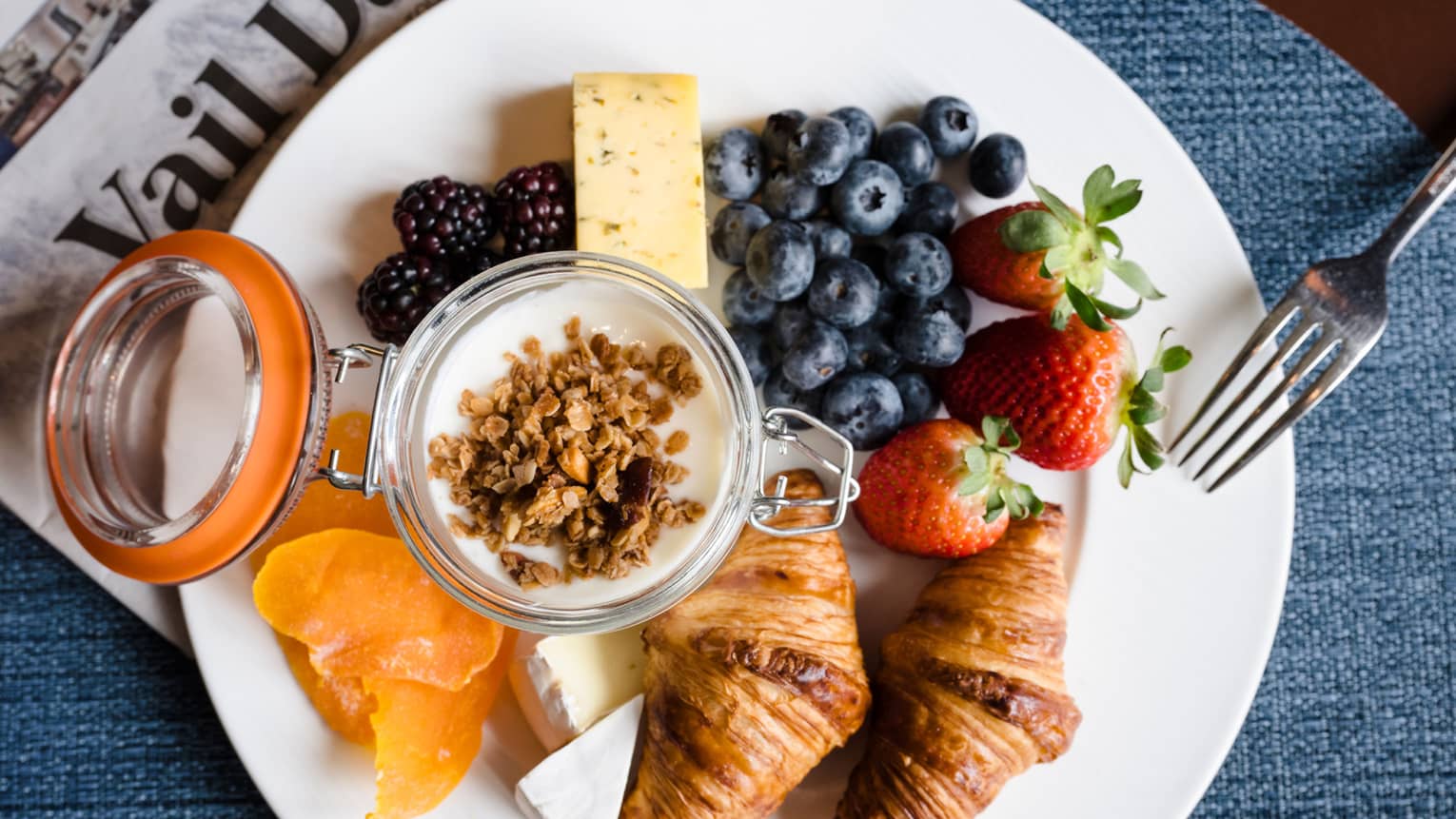 Plate of food with croissants, blueberries, strawberries and oranges.