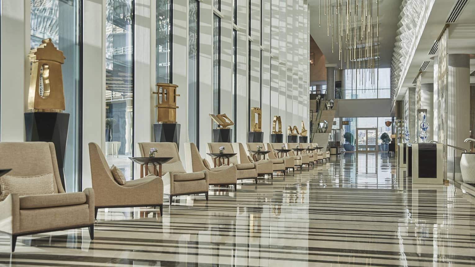 Hotel lobby with row of tan arm chairs, gold sculptures and floor-to-ceiling windows for natural light