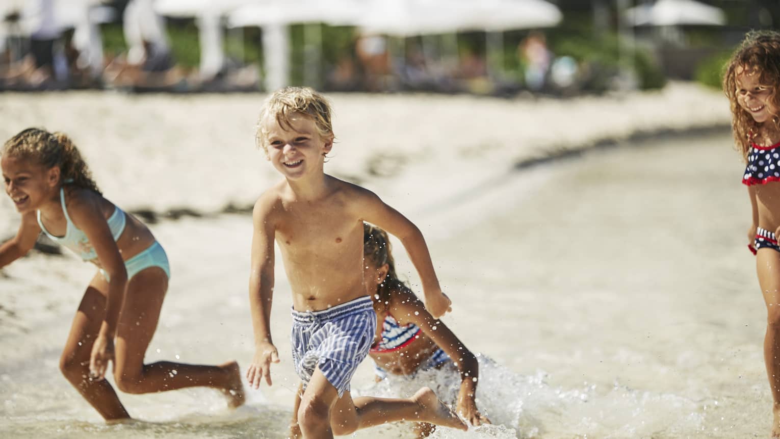 Kids in swimsuits run, laugh on sand beach