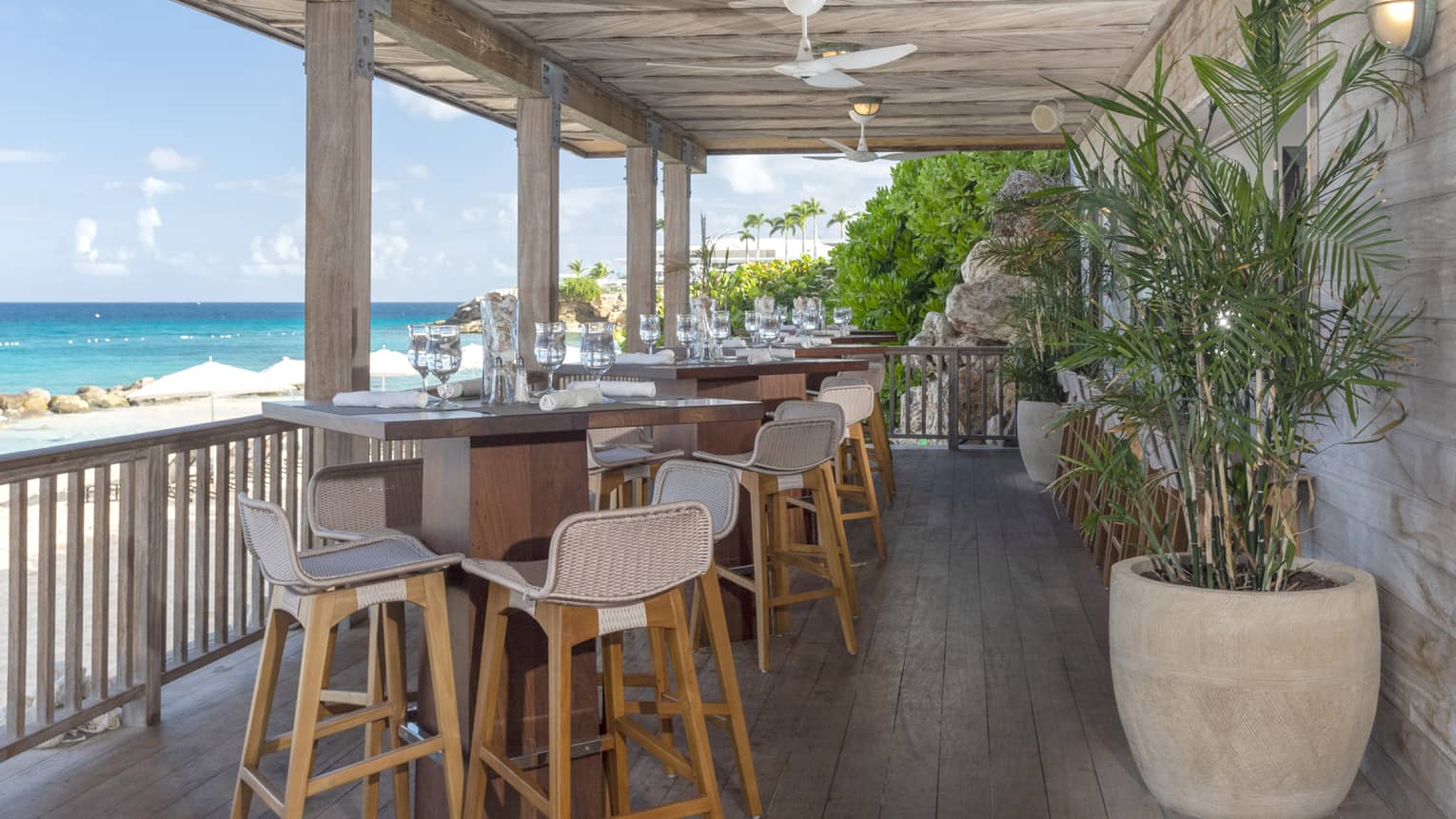 An open porch lounge set with cocktail tables and modern white and natural wood bar stools, overlooking the ocean at four seasons hotel anguilla