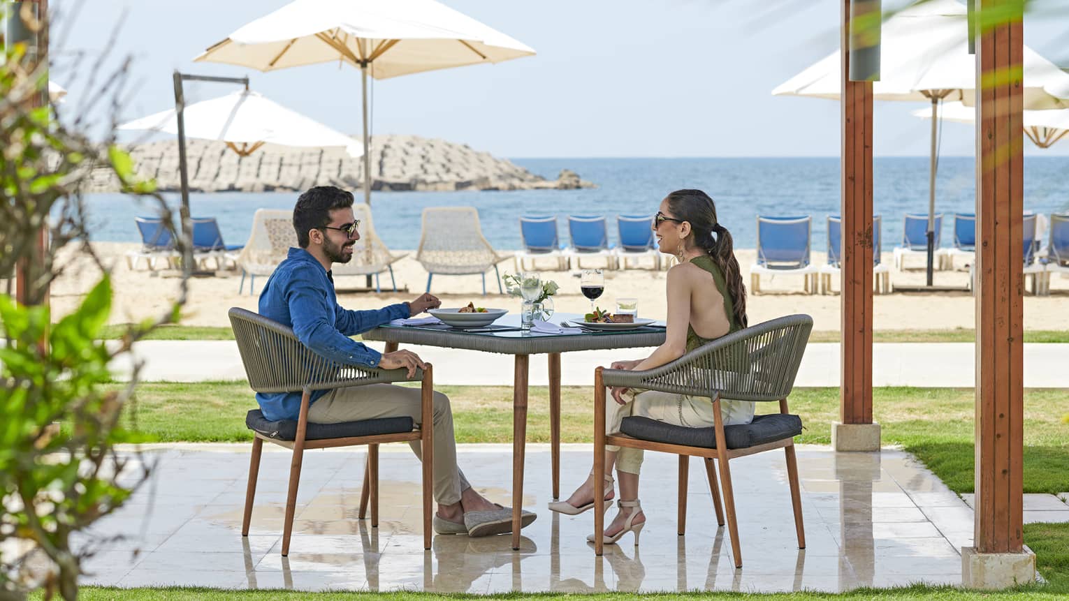 Smiling couple dines at patio table on private pergola near white sand beach