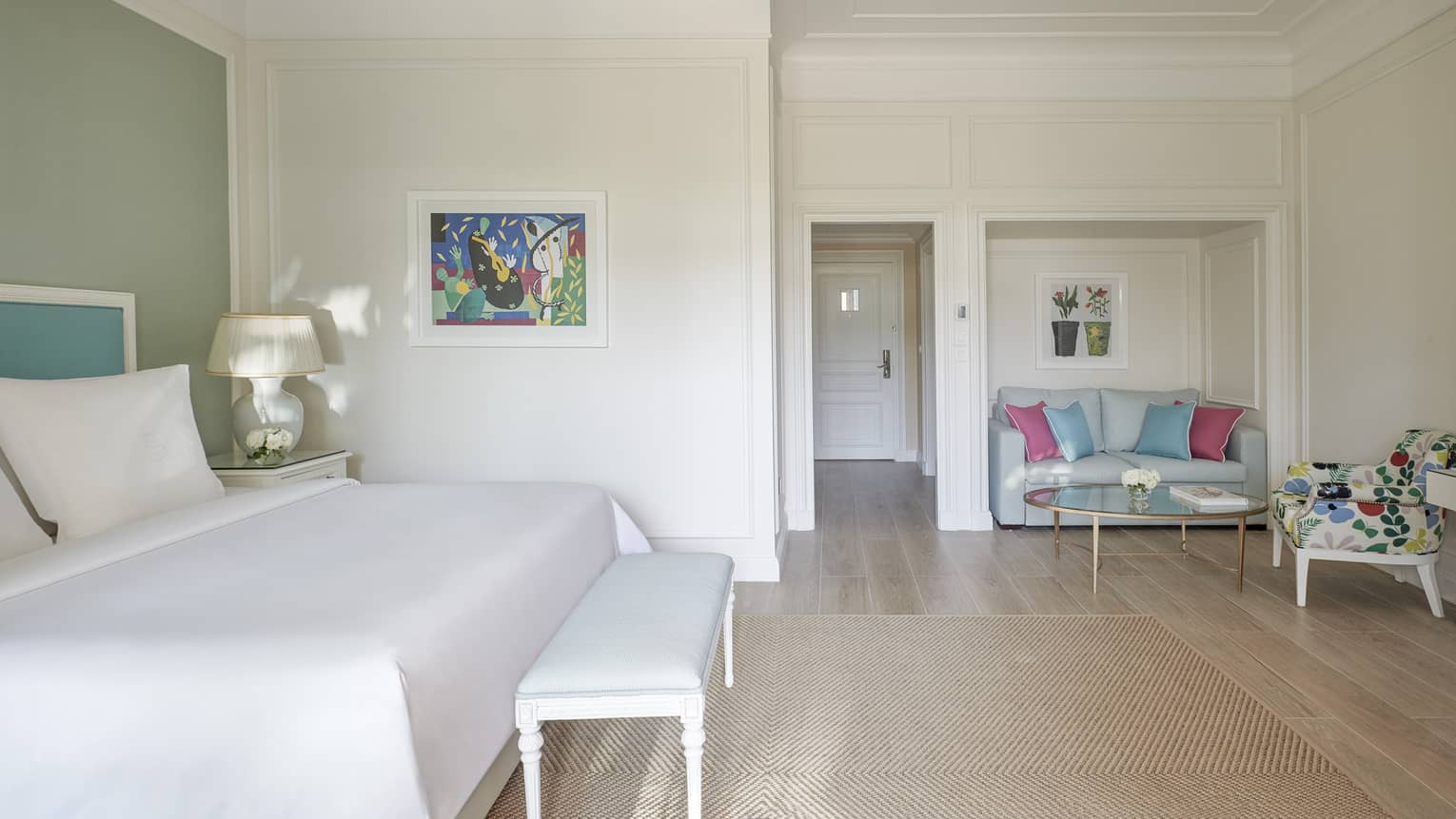 White room, white bed with blue headboard on green wall, foot bench, wood floor, seating area