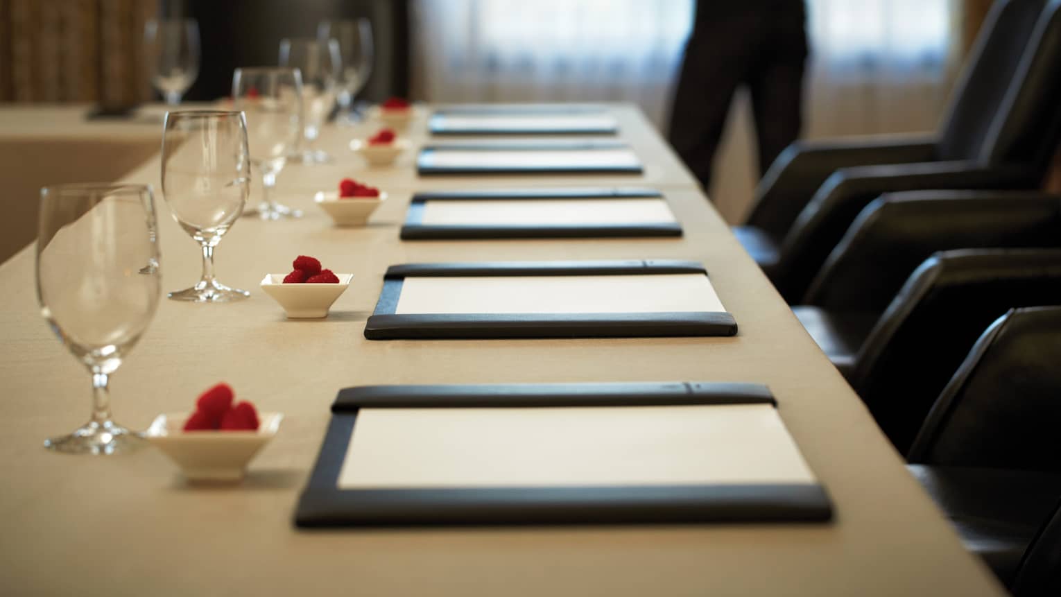 Rectangular meeting table with six place settings and a person standing in the background holding a tablet 