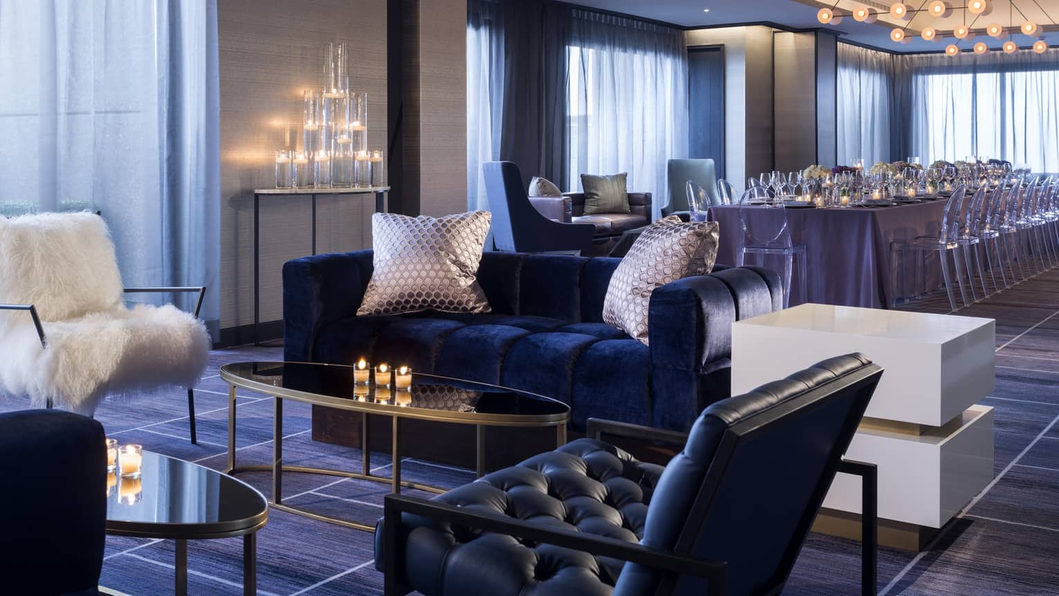 Penthouse seating area with blue velvet sofa, white faux fur chair by candles, long private dining table