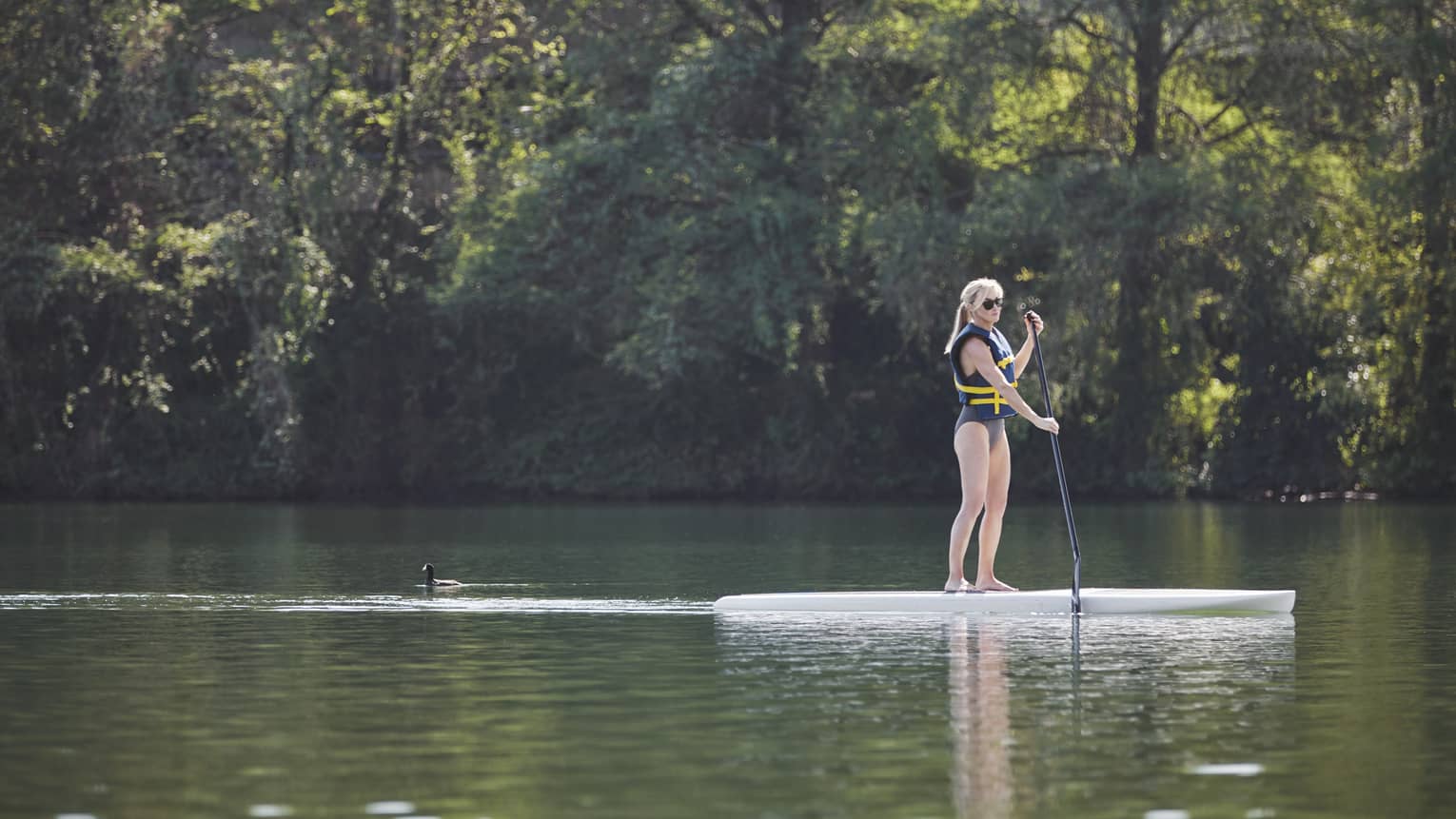 A woman paddle boards across serene waters