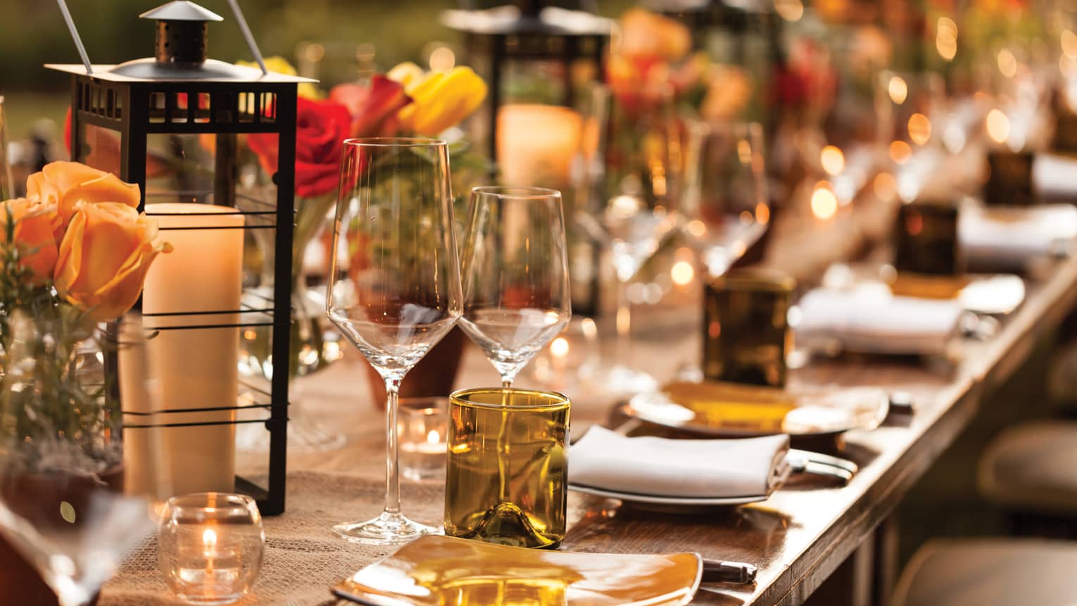 Table setting with orange, red and yellow flowers, wine glasses and candles.