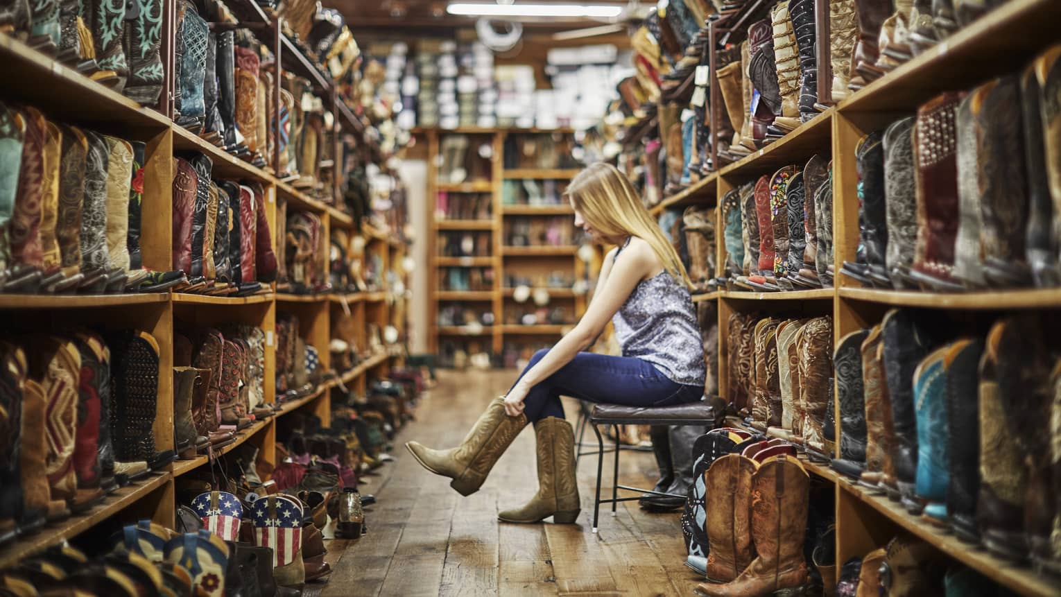 A woman trying on cowboy boots in a store full of them.
