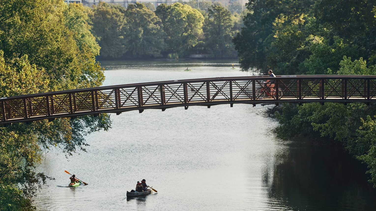 People in kayak, canoe on lake under cyclist on foot bridge