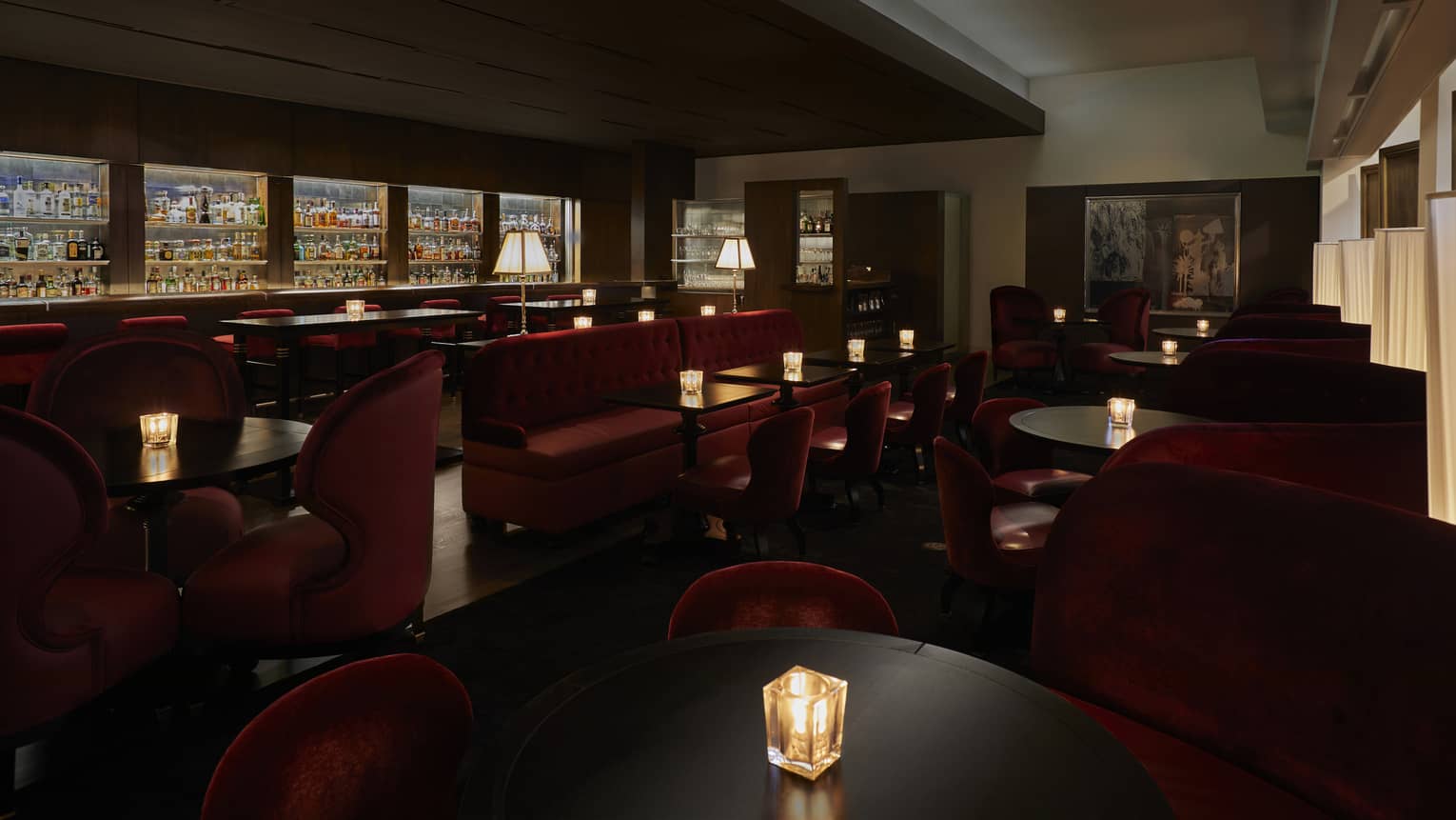 A dimly lit lounge with red chairs and a large selection of drinks behind a bar.