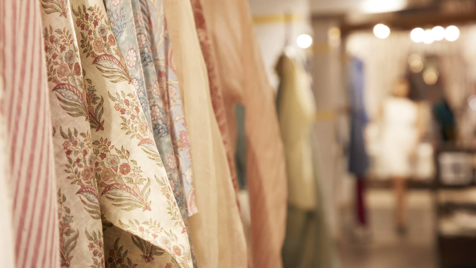 Close up of garment sleeves hanging on a clothing rack, featuring various solid, striped and floral textiles in peach, cream and gold tones