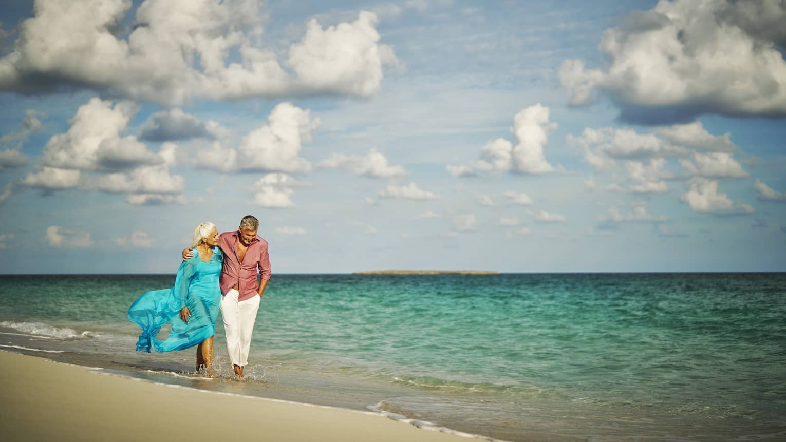 Couple walking on the shore of the beach with the blue sky behind them.