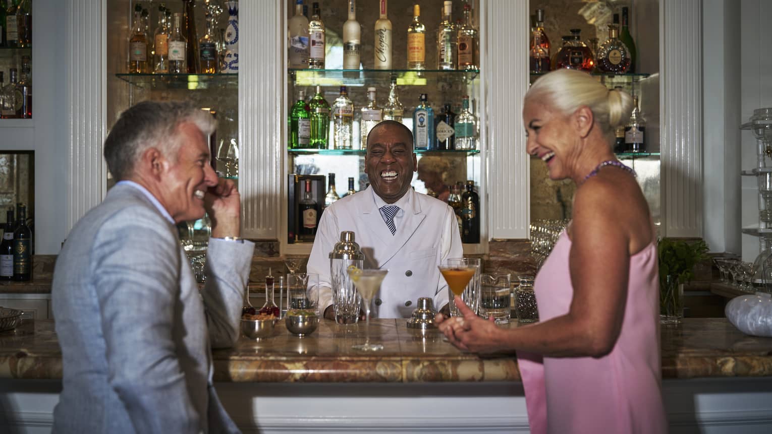 Man and woman standing at the bar, laughing together with the bartender.