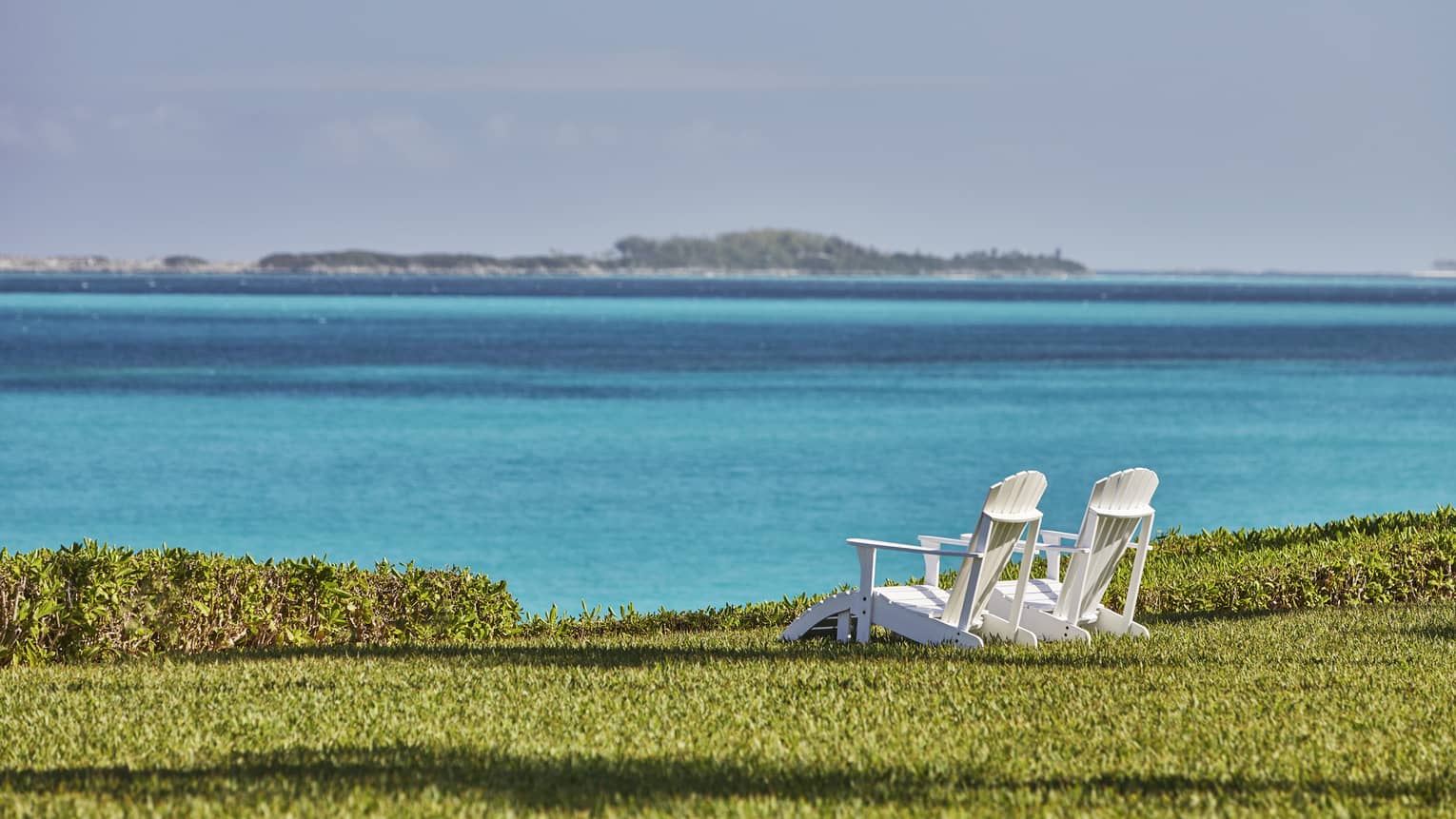 Two white patio chairs on green Crescent Lawn overlooking ocean