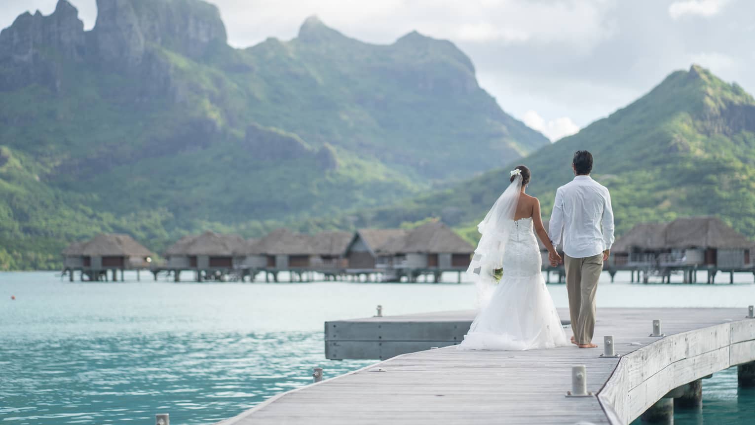 Bride and groom on overwater bungalow walkway, Bora Bora mountains in background