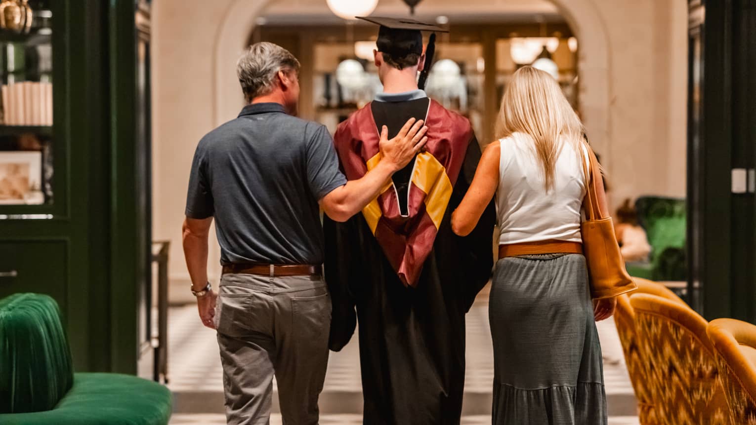 Parents walking with child in graduation gown.