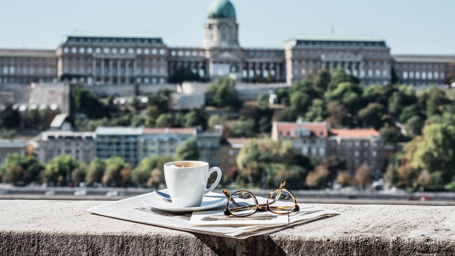 Morning view of Buda Castle from guest room terrace, cup of coffee, eyeglasses on rail