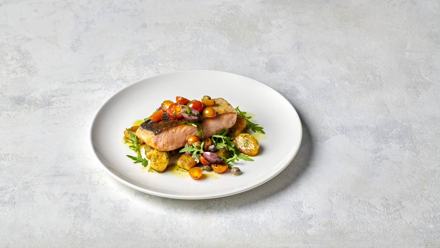 Pan-seared Salmon on white plate with Pesto Gnocchi, Wilted Rocket and Vierge Dressing
