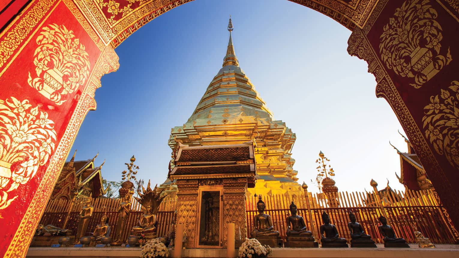 View from under painted arch looking up at golden Wat Phra That Doi Suthep historic Buddhist temple, statues 