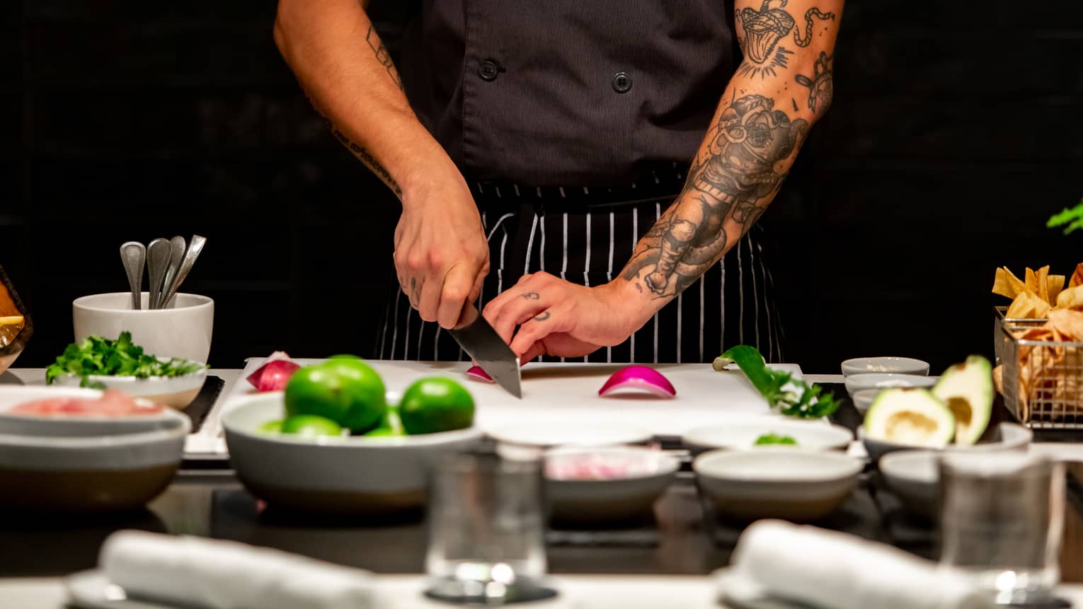 Close up of chef with tattoos on his arm slicing a red onion