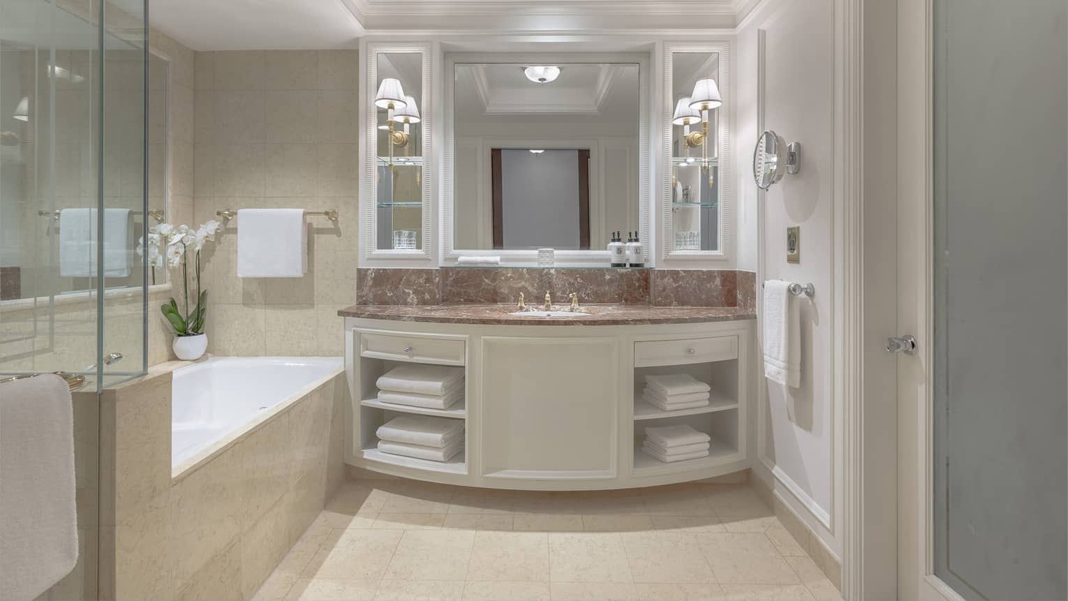 A bathroom with a counter with sink, shelves for towels, an enclosed shower and bathtub.