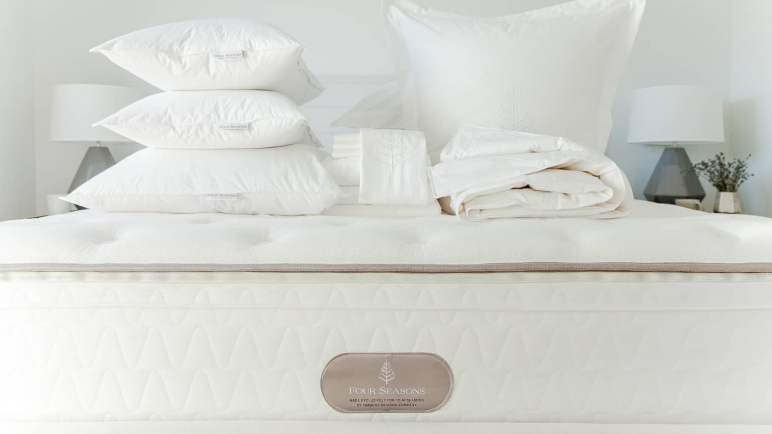 Queen bed stacked with folded white linens and feather pillows