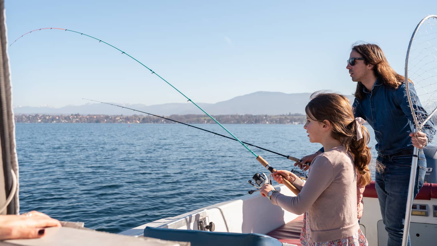 Man holding net and fishing rod, and girl standing in boat, holding fishing rod