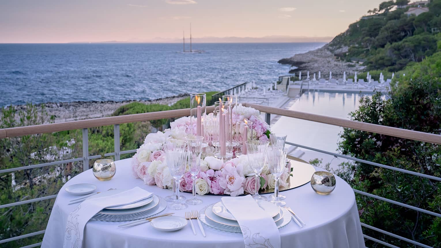 Balcony with round set table, pink floral arrangement, water views at sunset