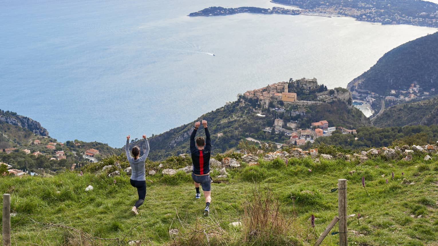 Rear view of woman and man doing yoga on green hilltop overlooking Mediterranean Sea