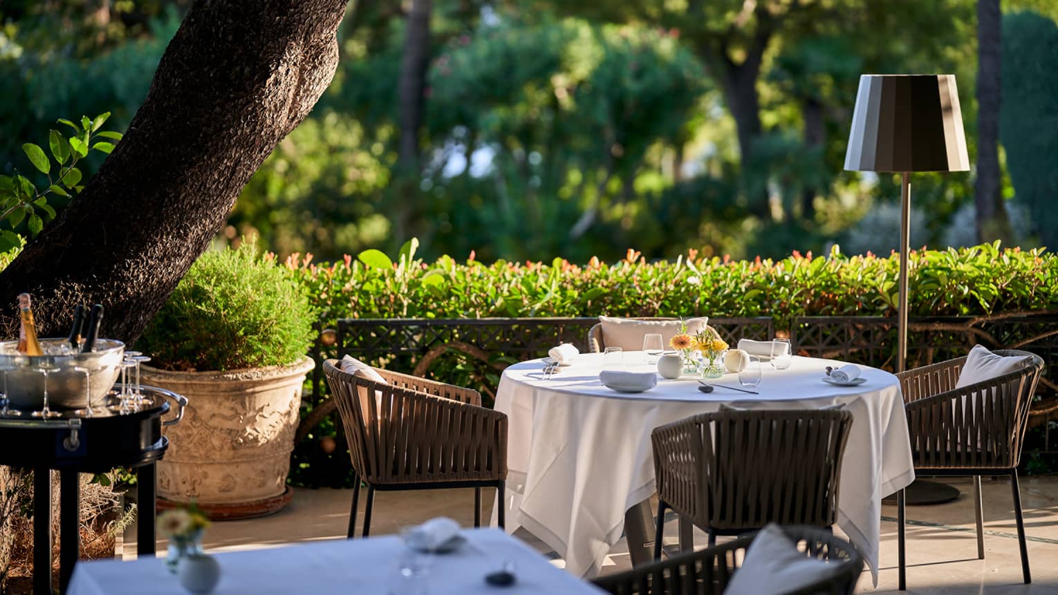 Le Cap restaurant terrace with Champagne stand, white round table, rattan chairs, hedge