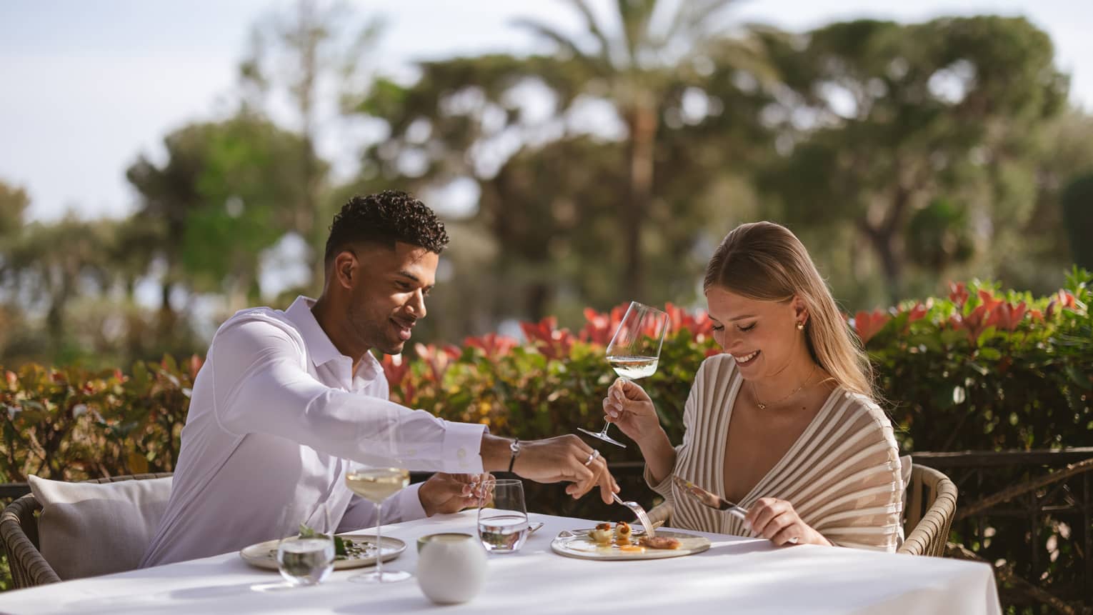 Couple smiling over dinner on elegant patio with palm trees in backdrop