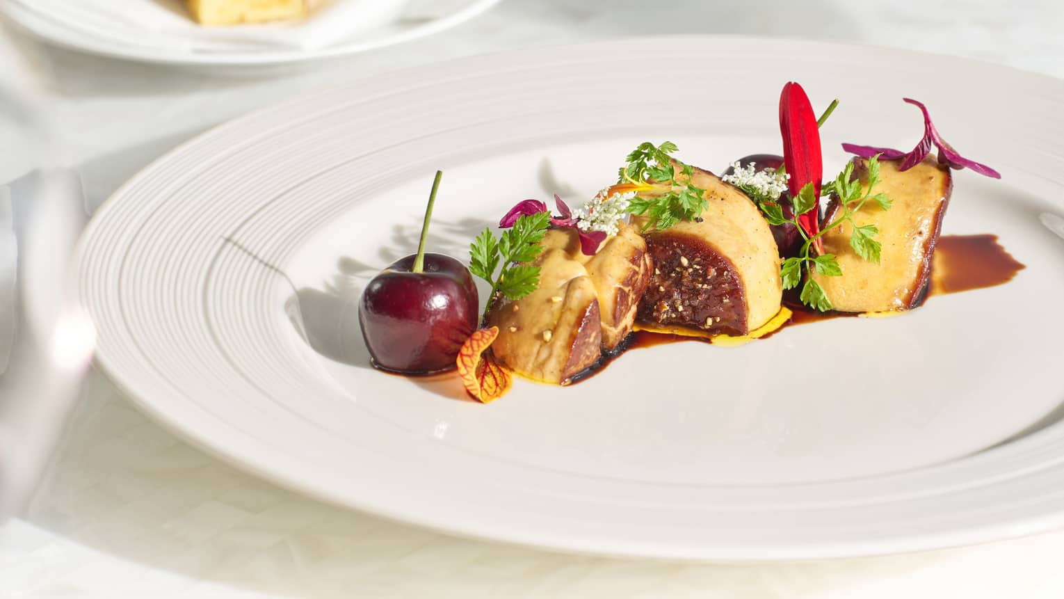 Delicately arranged foie gras garnished with microgreens; deep red, magenta and white flower petals; balsamic; and a cherry.