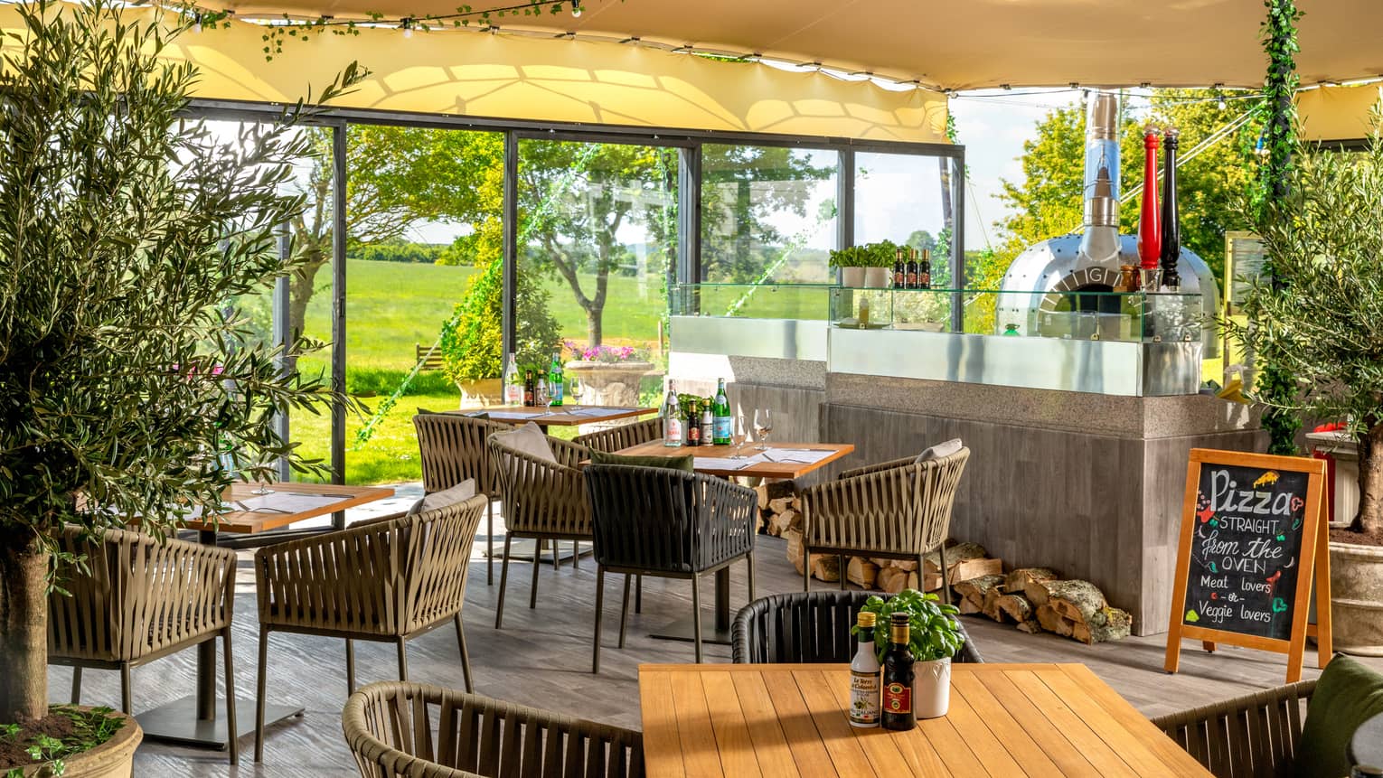 A well lit dining outlet with large windows, wood chairs and plants.