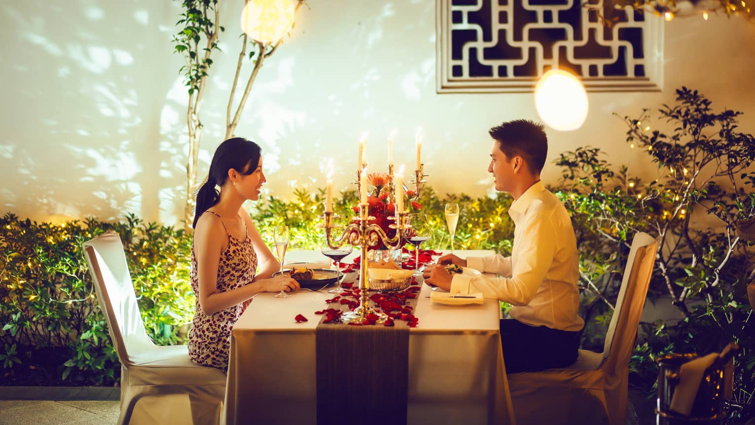 Couple at candle-lit private dining table with red rose petals on villa patio