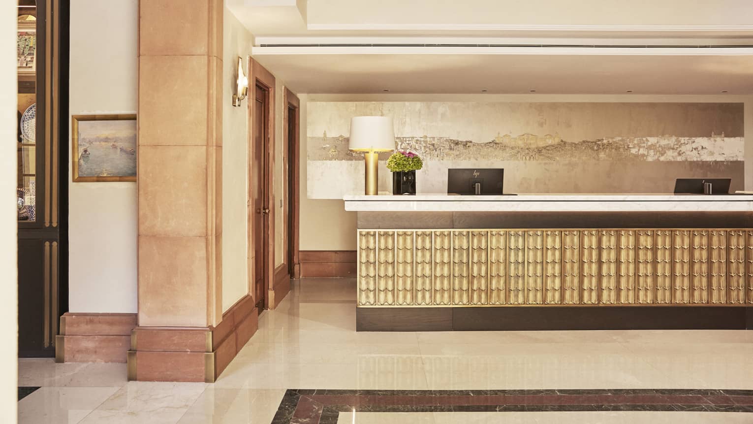 The lobby of a hotel with beige colouring and a large counter with computer screens.