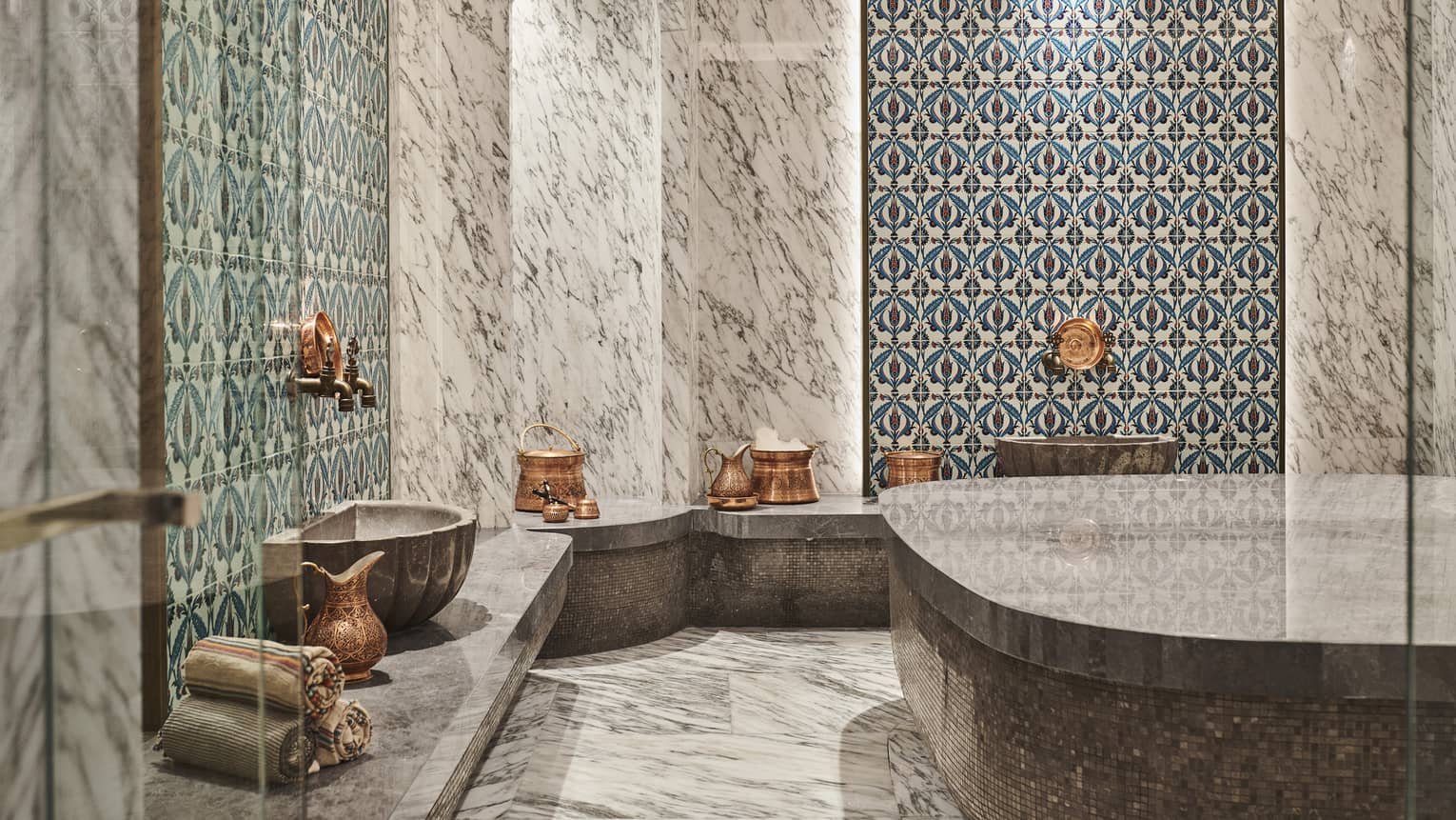 Steam shower with mosaic tile and full marble walls, floor and benches, and brass urns