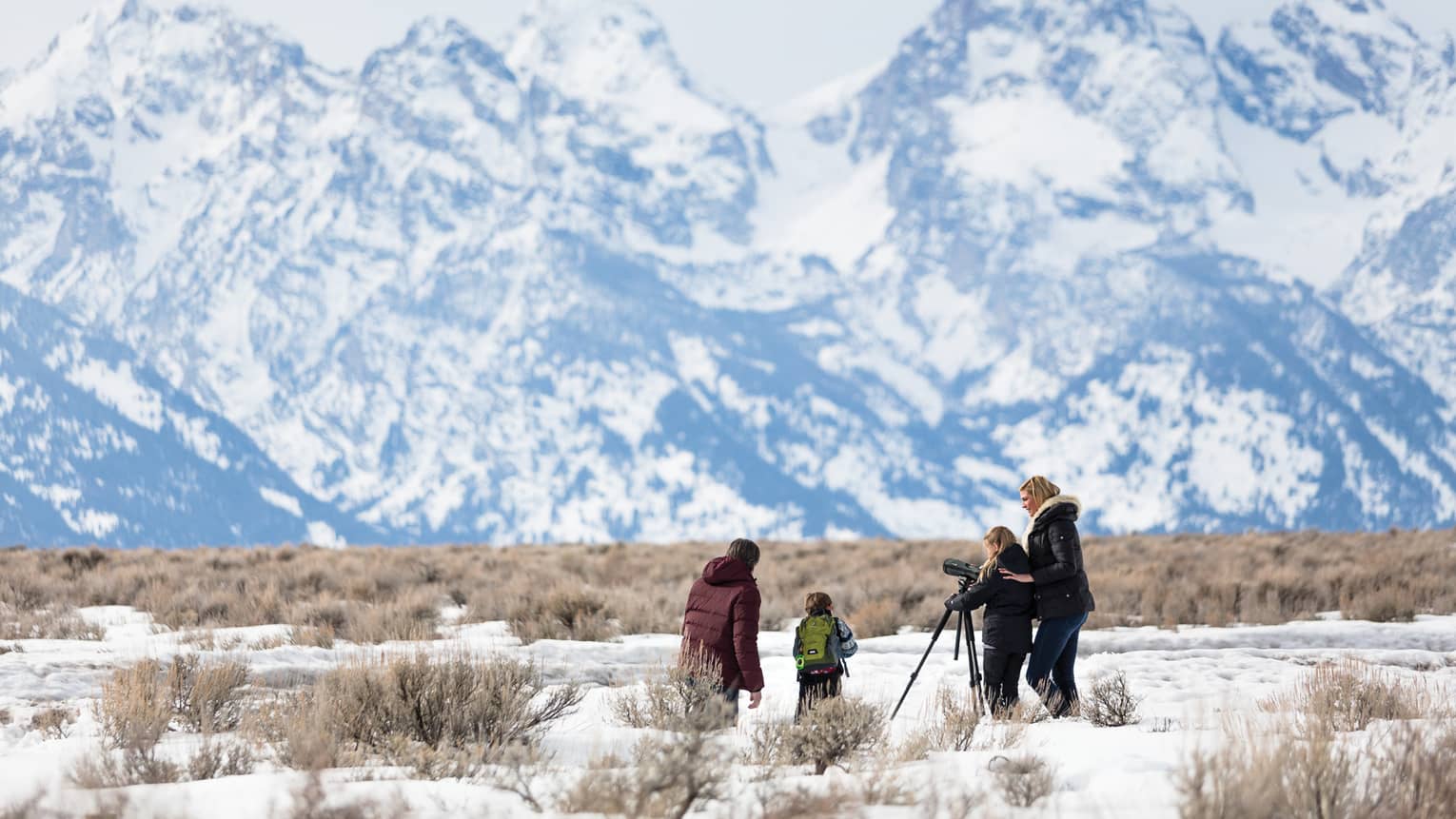Family in snowy field with camera on tripod pointed at towering mountains