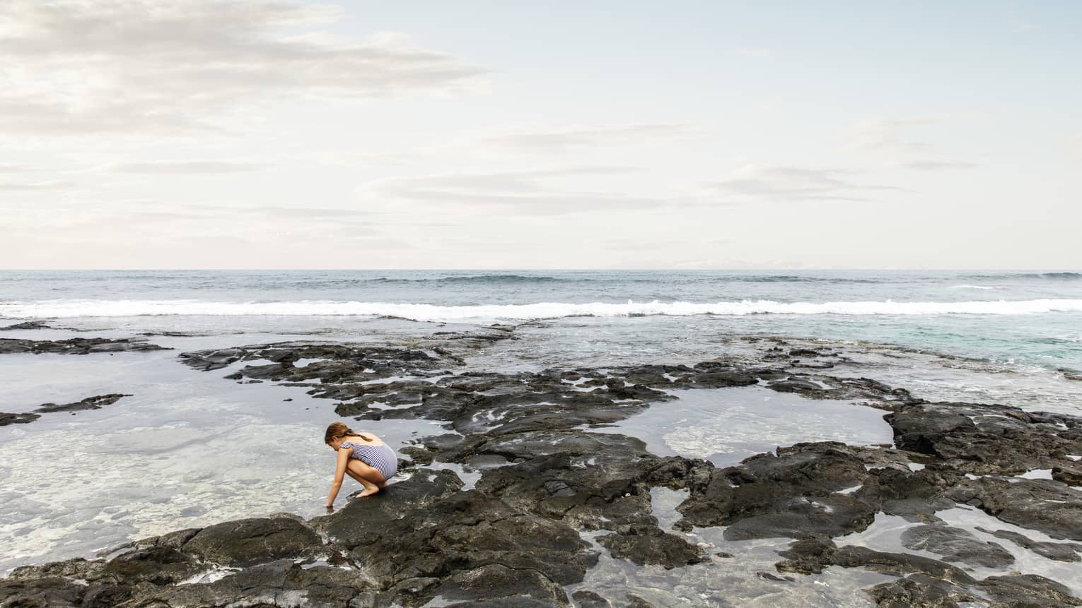 A young guest kneels in the shallow waters on a Hualalai beach