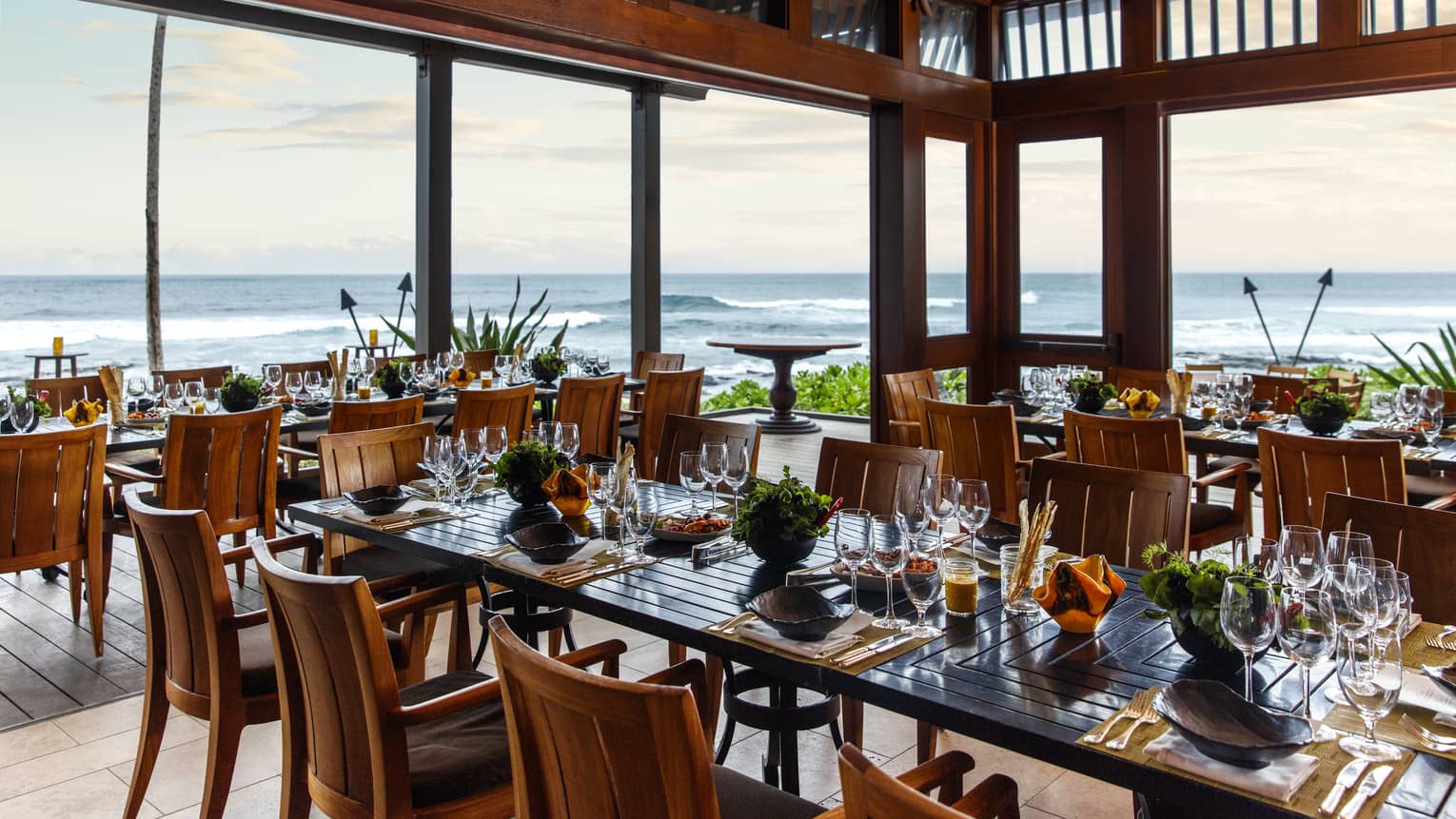 Restaurant dining tables under wood awning in open air room overlooking ocean