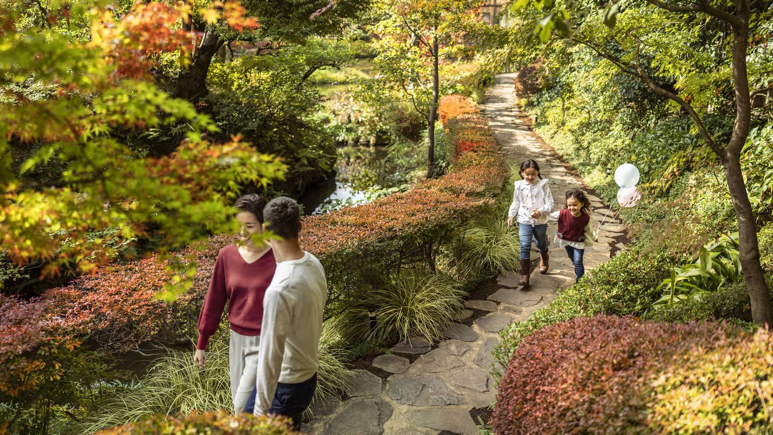 Couple and their two daughters walk along foliage-lined pathway parallel to the koi pond