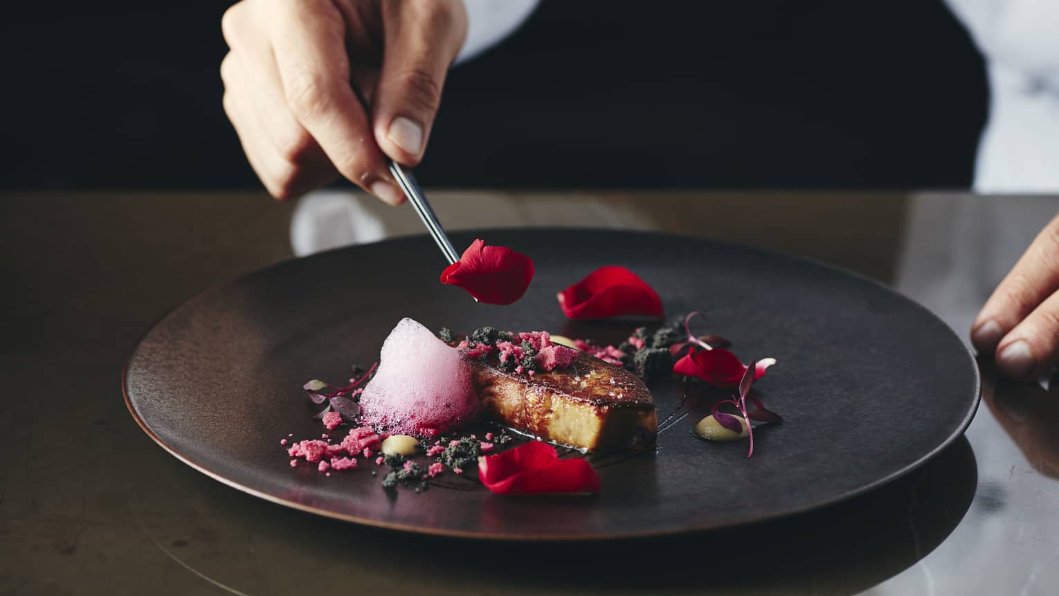 Chef places rose petal on small gourmet dessert