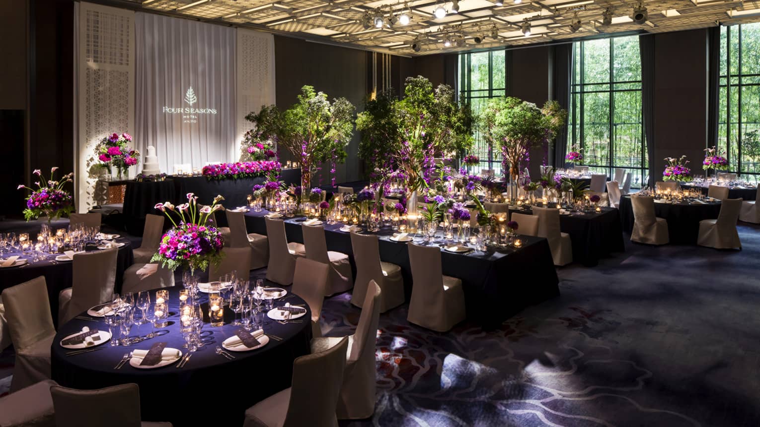 Wedding reception banquet, tables set with purple linens and flowers, under modern ceiling with lights