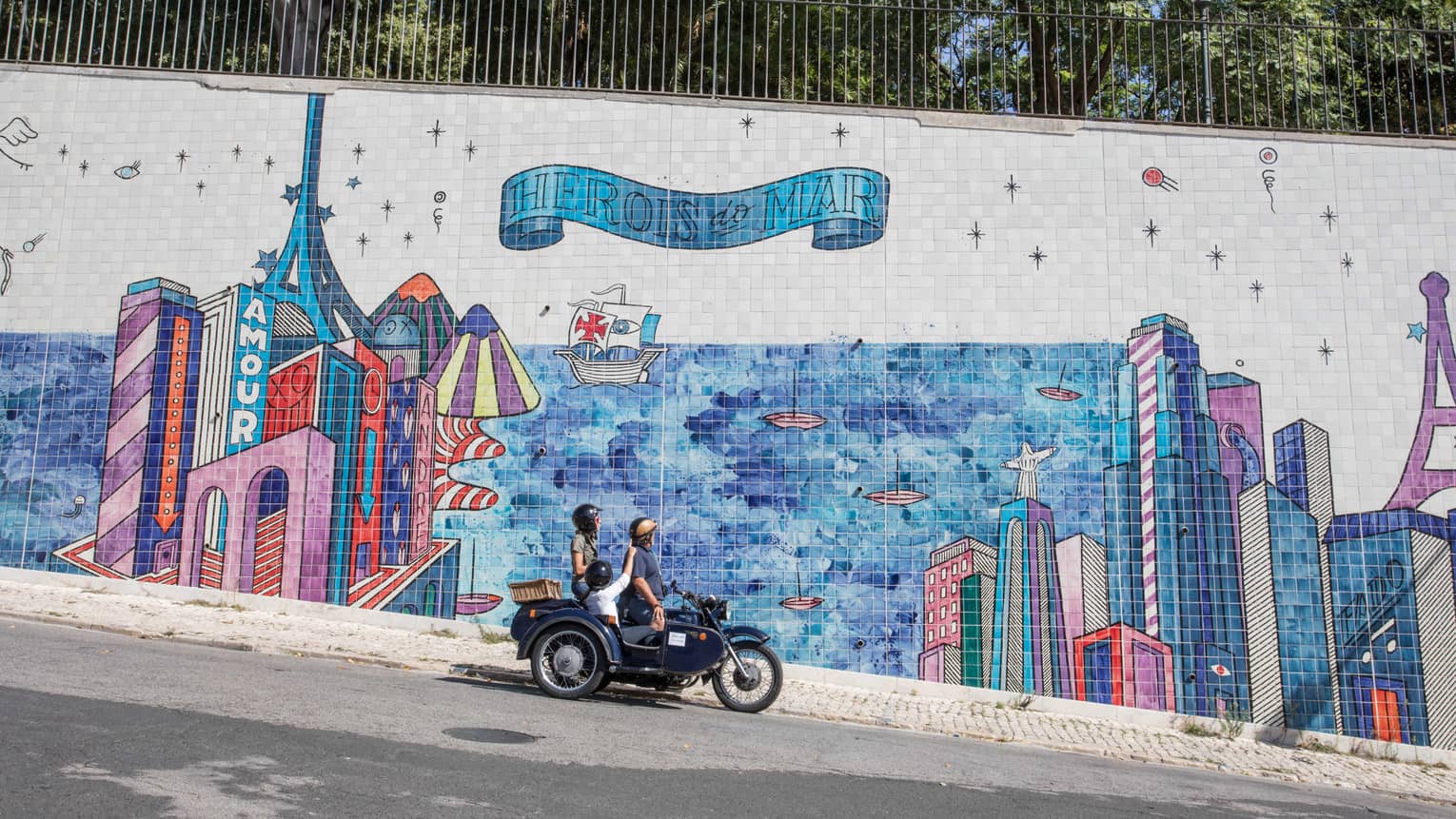 Two adults and a child stop their motorcycle to look at a city mural made of tiles