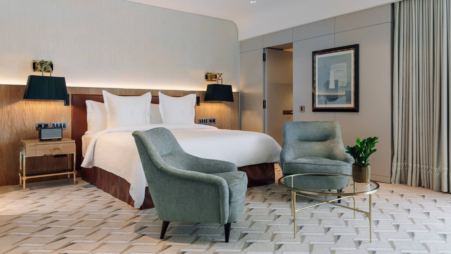Hotel room with king bed, two turquoise arm chairs and brass glass table