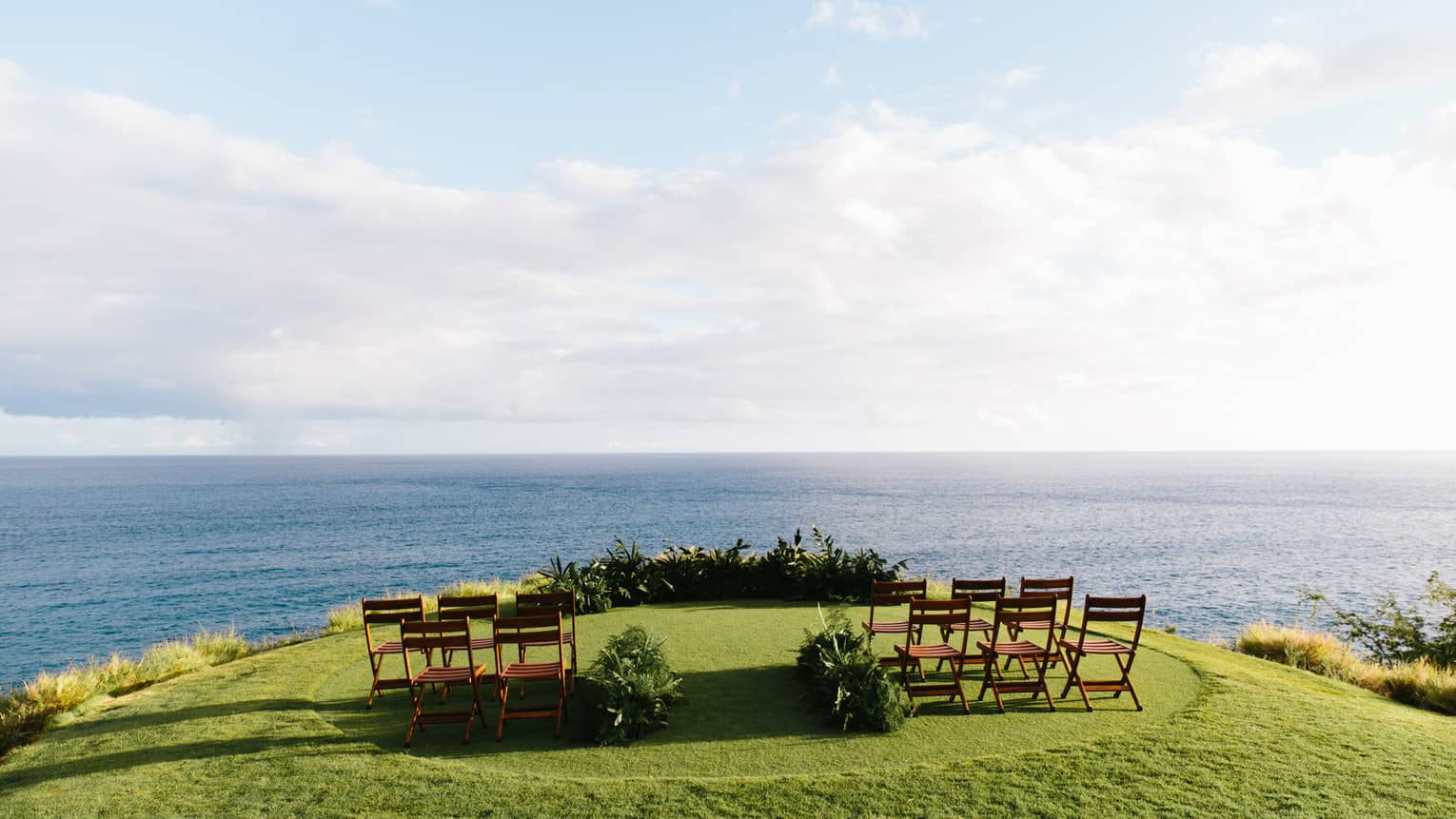 A series of wooden chairs set up on a green golf course overlooking a calm blue sea.